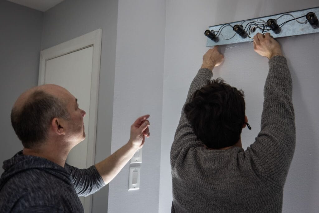 As one of the last steps in a bathroom renovation in Rockland, a man is installing a light fixture on the wall, carefully positioning it for optimal illumination in the room.