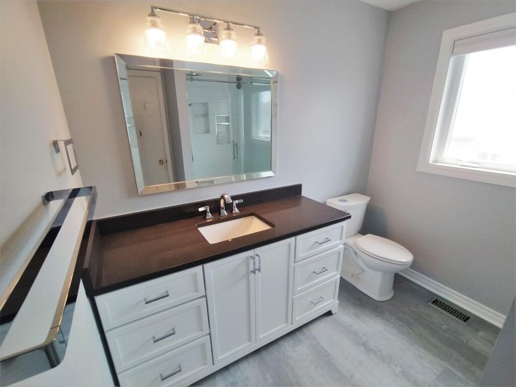 A completed bathroom renovation project in Rockland featuring a sink, toilet, and mirror, showcasing a modern and functional design.