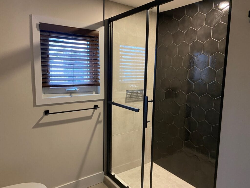 A stylish shower in Nepean enclosed by a glass door, complemented by a black honeycomb tile on an accent wall, offering a modern and elegant design.